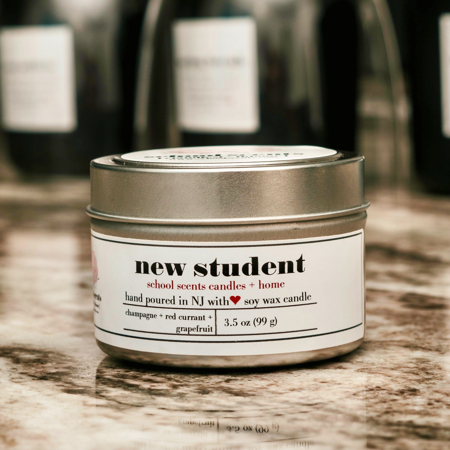 Close up of silver travel tin candle labeled “New Student” on a marble surface