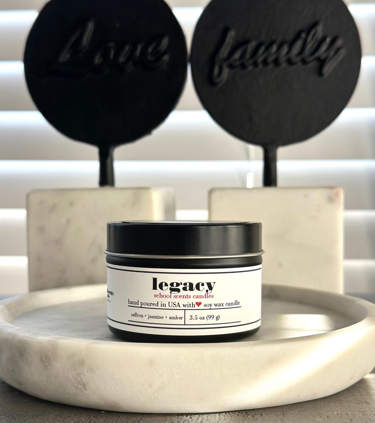 Black travel tin candle labeled “Legacy” on a marble surface