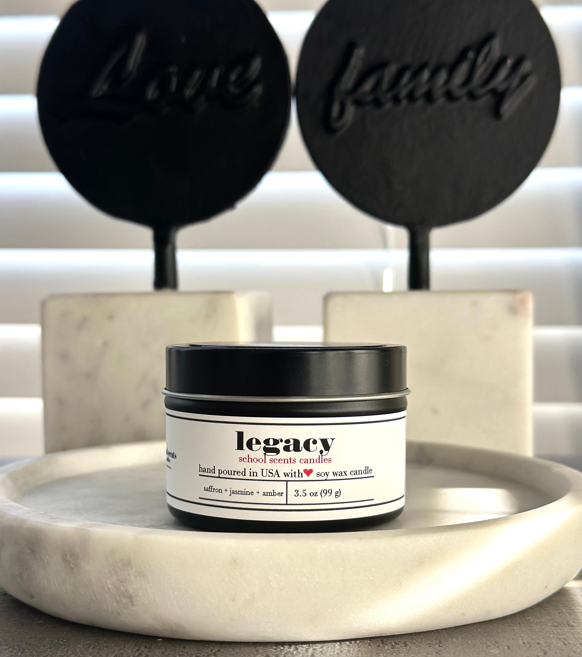 Black travel tin candle labeled “Legacy” on a marble surface