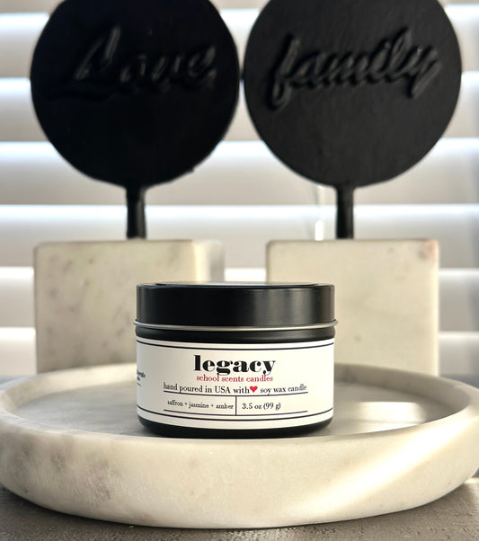 Black travel tin candle labeled “Legacy” on a marble surface