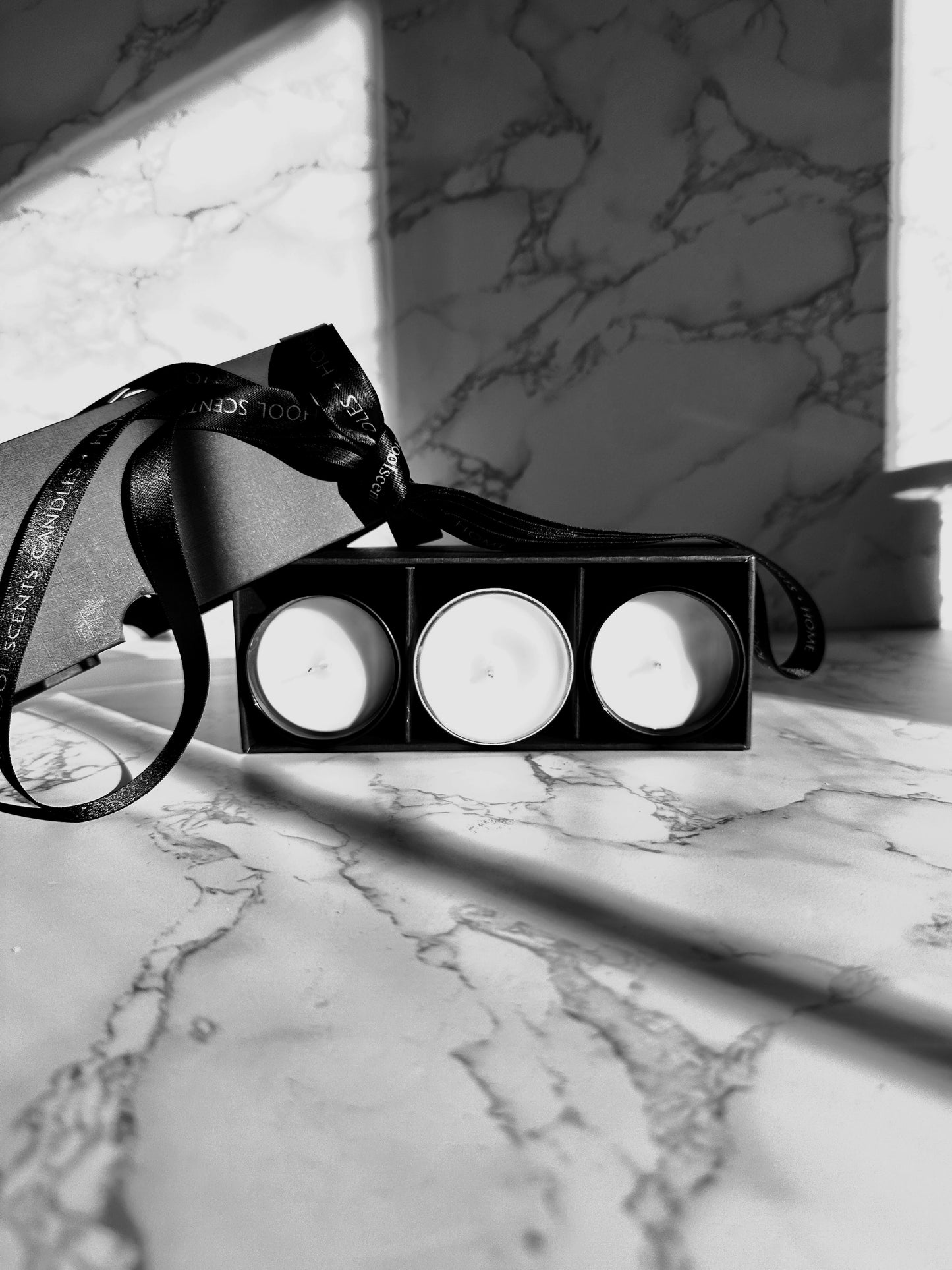 Mini candle gift set with three tins in a black box tied with ribbon on a marble surface
