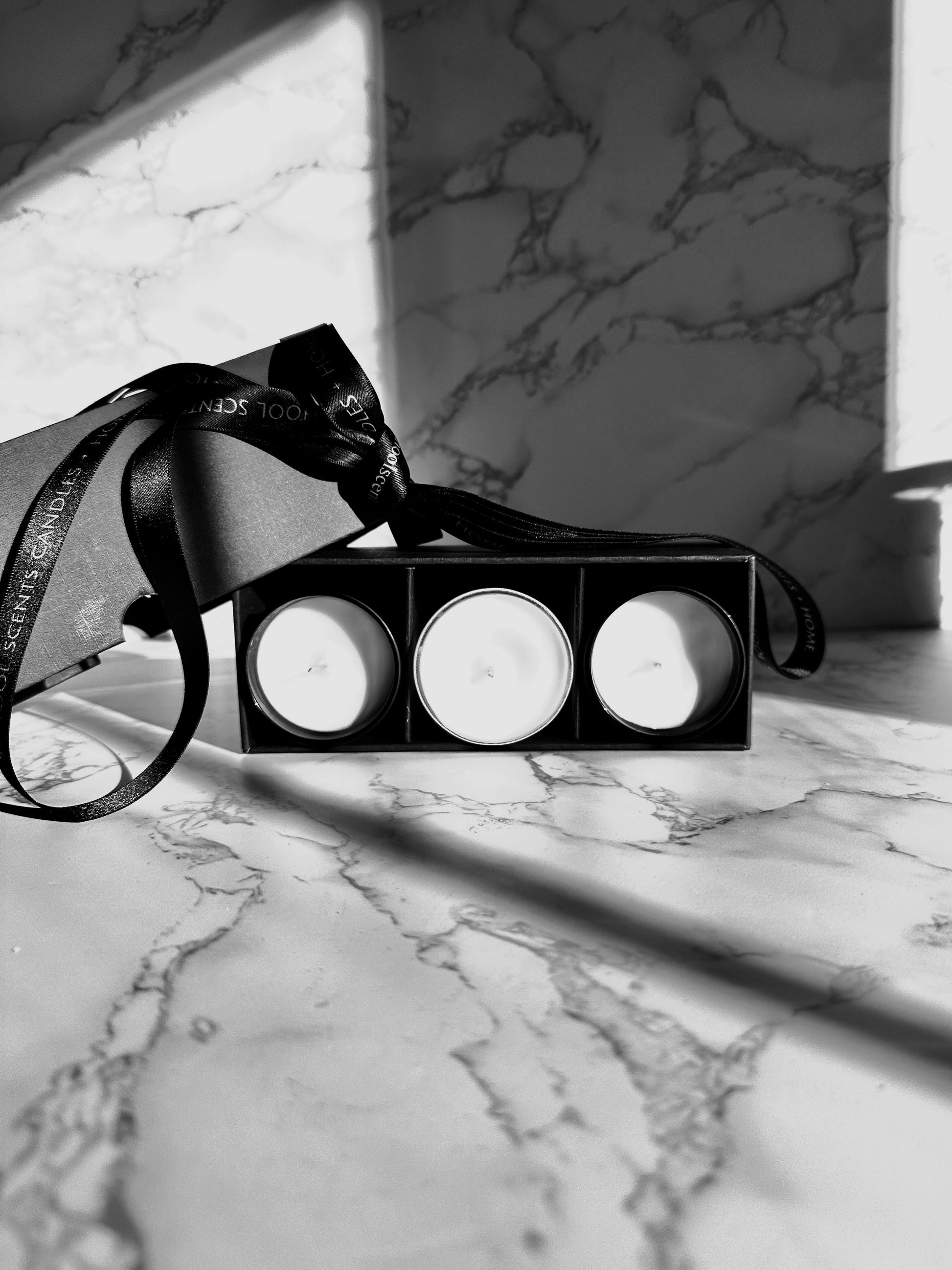 Mini candle gift set with three tins in a black box tied with ribbon on a marble surface