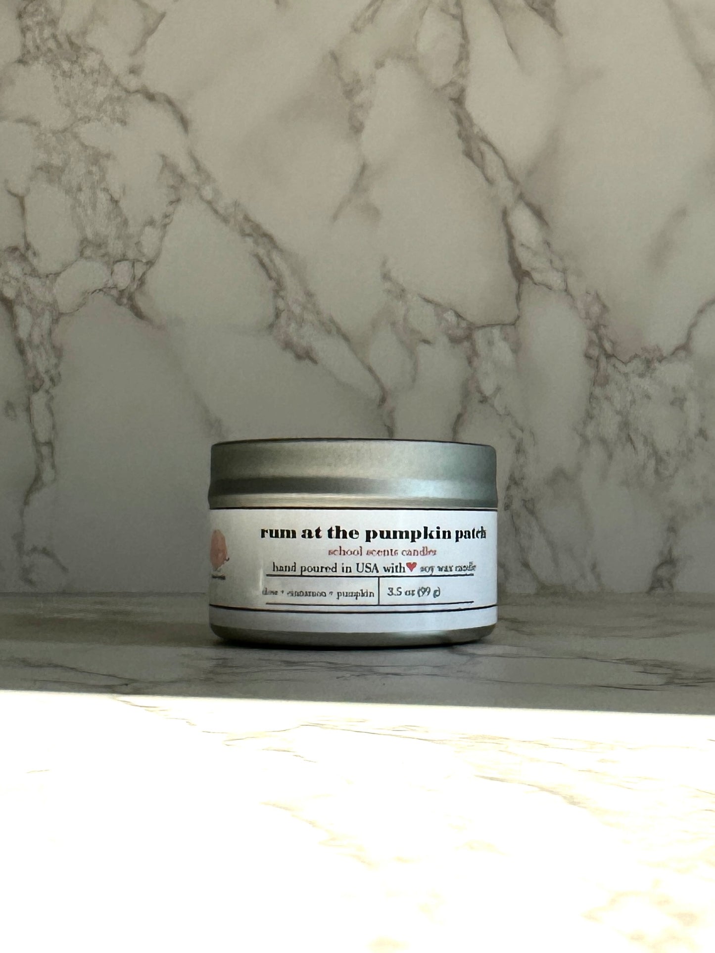 Silver travel tin candle labeled “Run at the Pumpkin Patch” on a marble surface