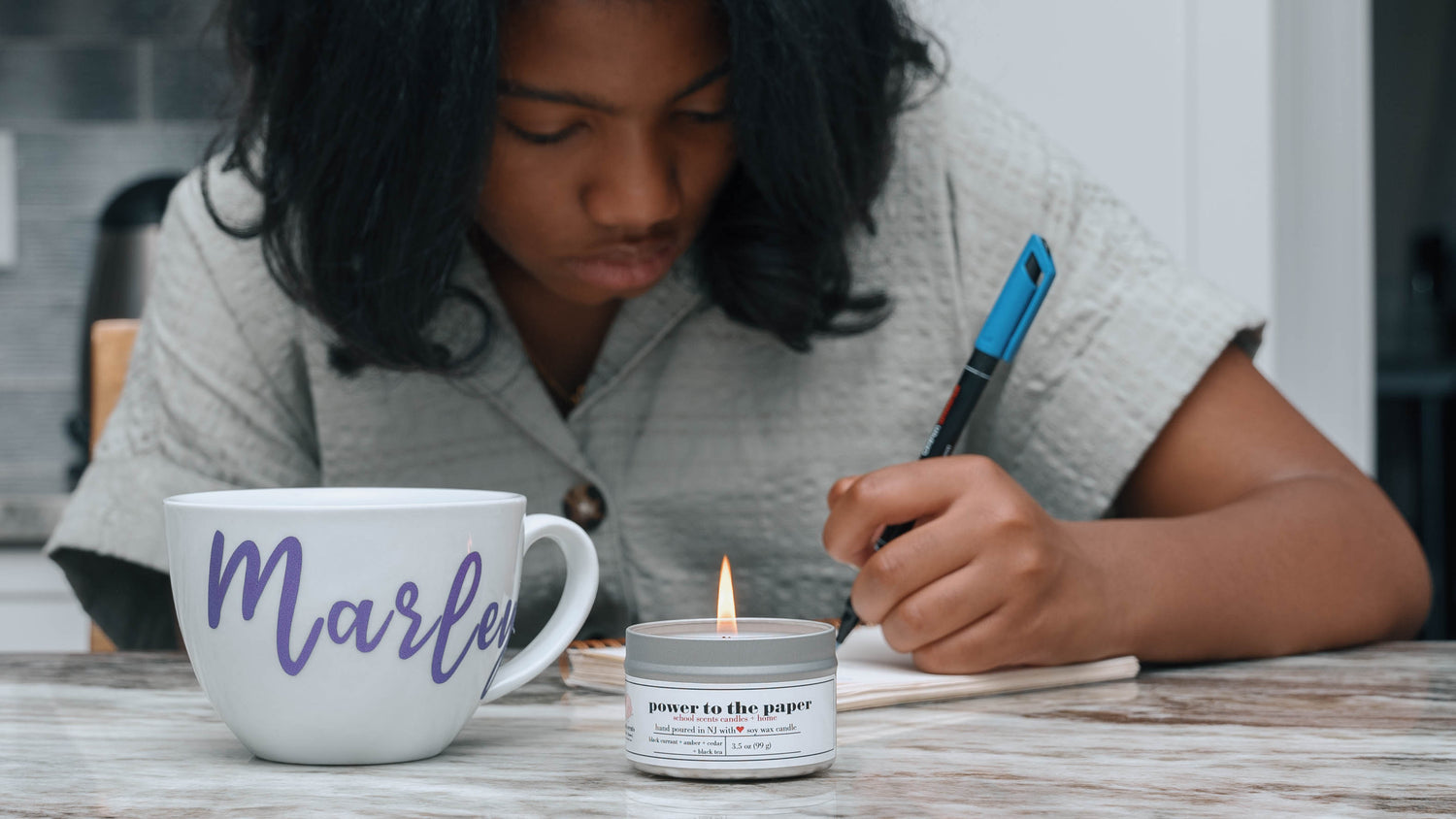 Girl writing in a notebook beside a personalized mug and lit candle from School Scents
