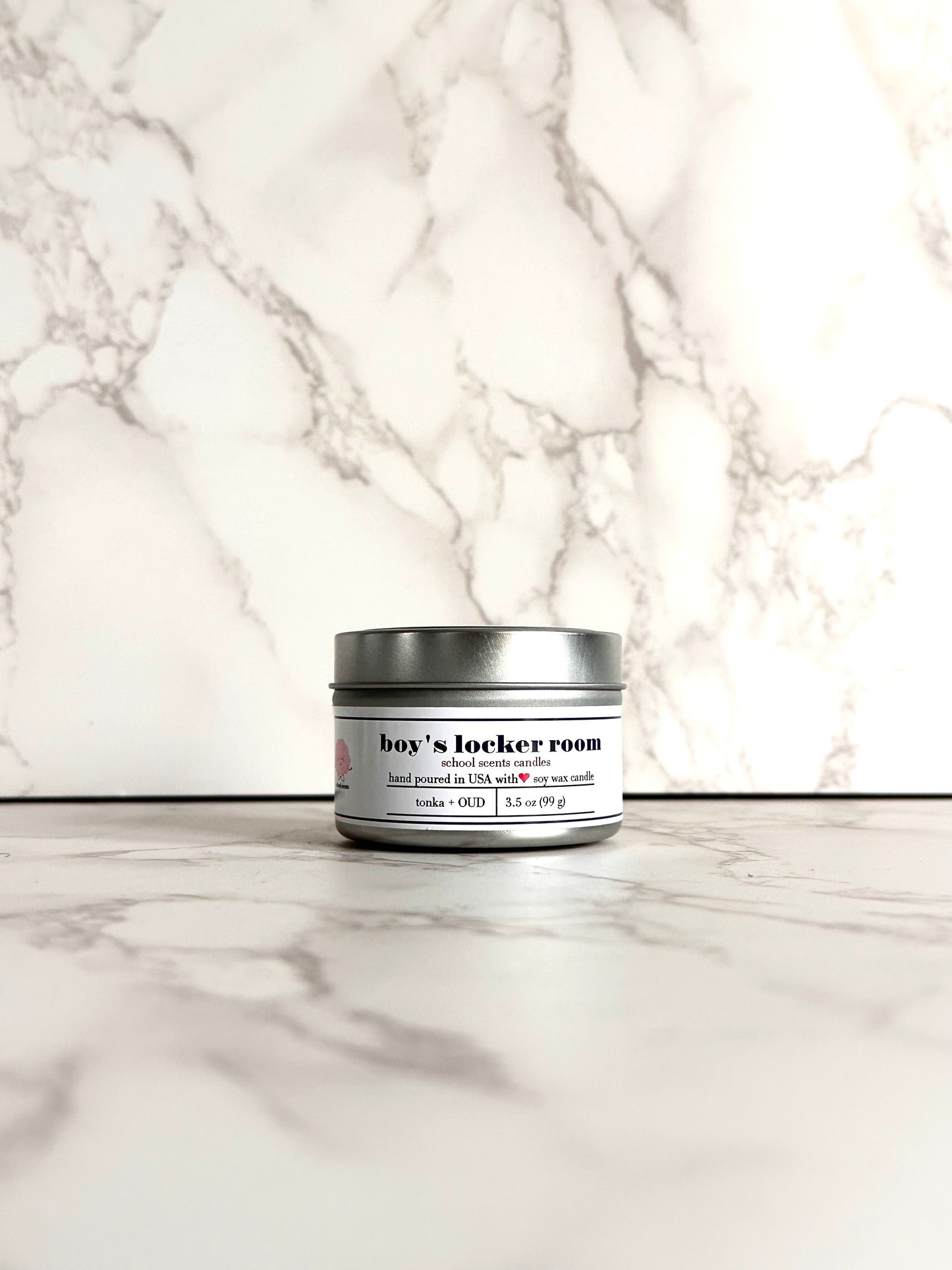 Silver travel tin candle labeled “Boys Locker Room” on a marble surface