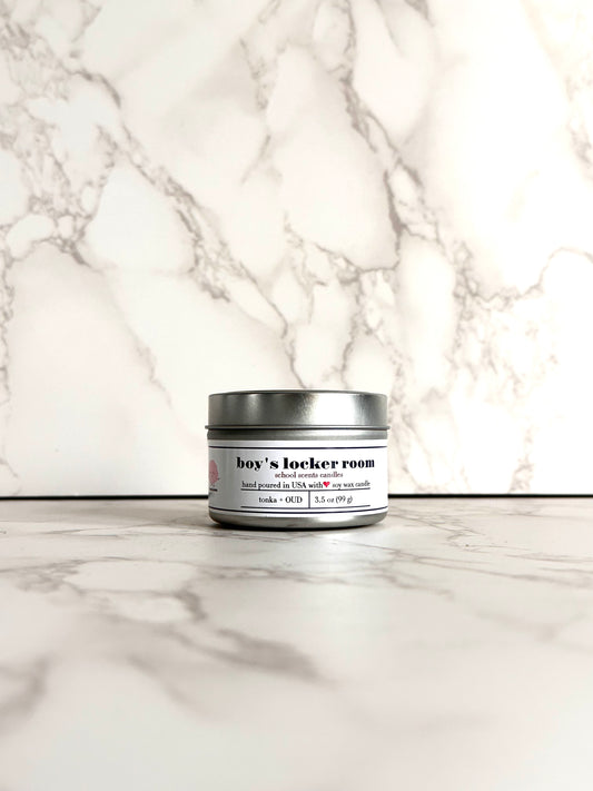Silver travel tin candle labeled “Boys Locker Room” on a marble surface