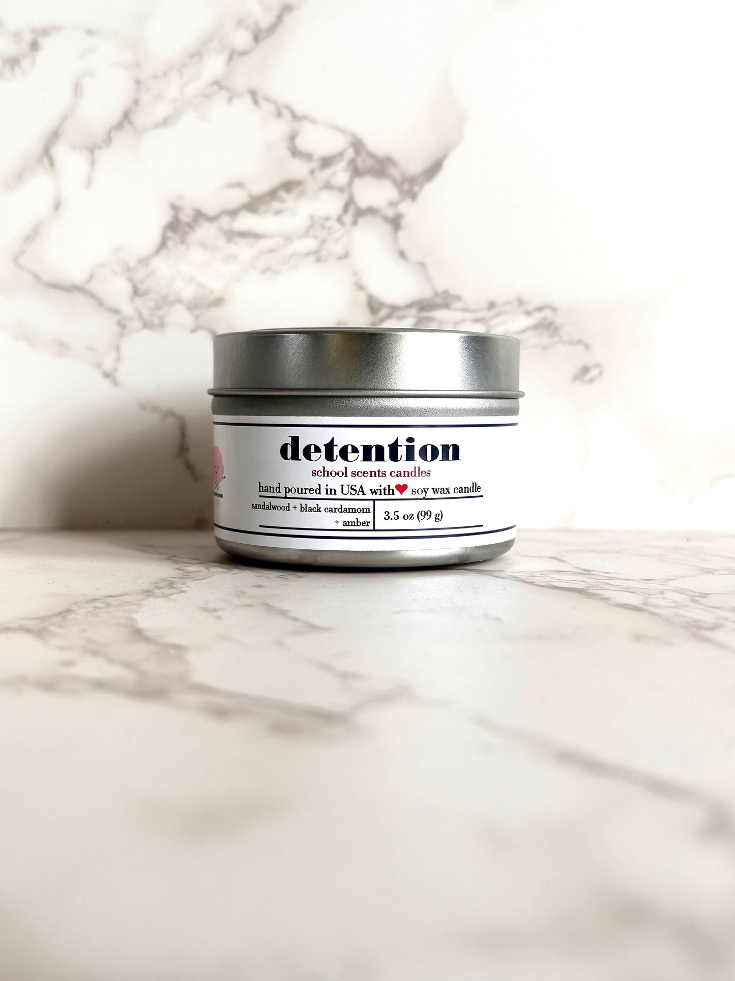 Silver travel tin candle labeled “detention" on a marble surface