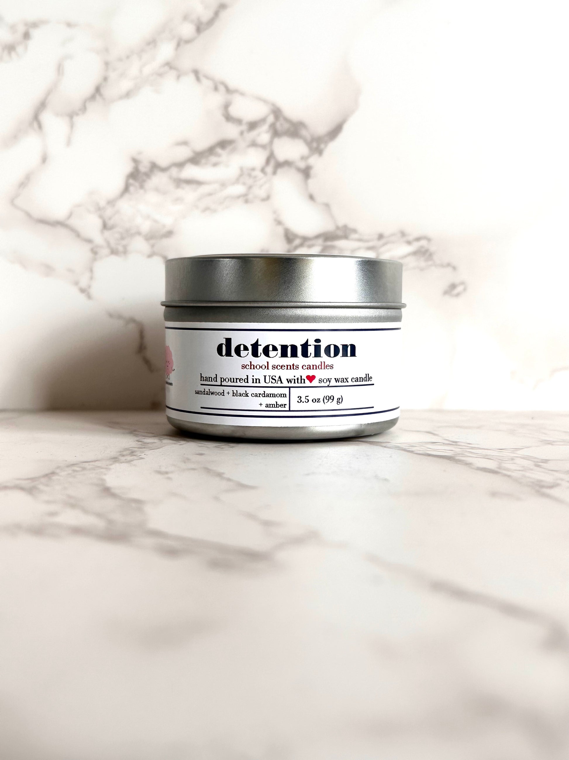 Silver travel tin candle labeled “detention" on a marble surface
