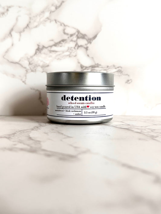 Silver travel tin candle labeled “detention" on a marble surface
