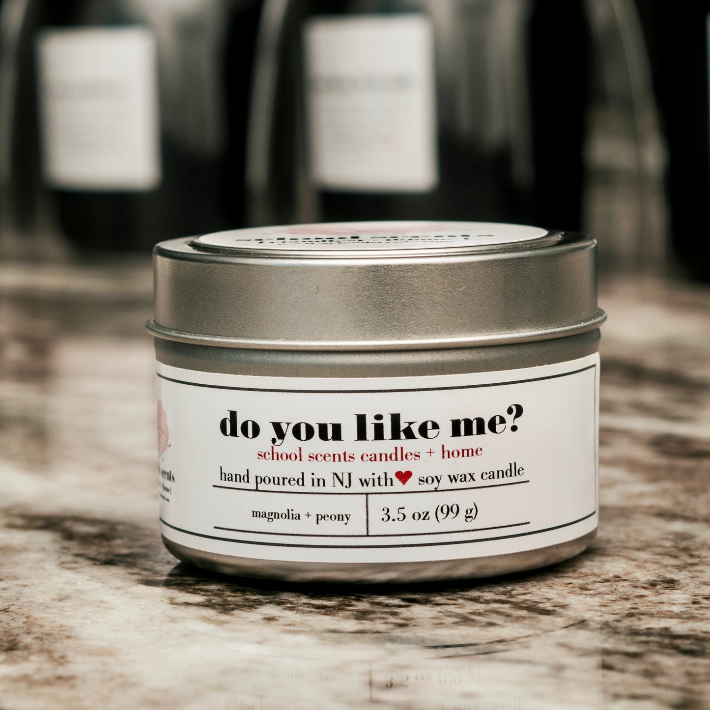 Close up of silver travel tin candle labeled “do you like me" on a marble surface