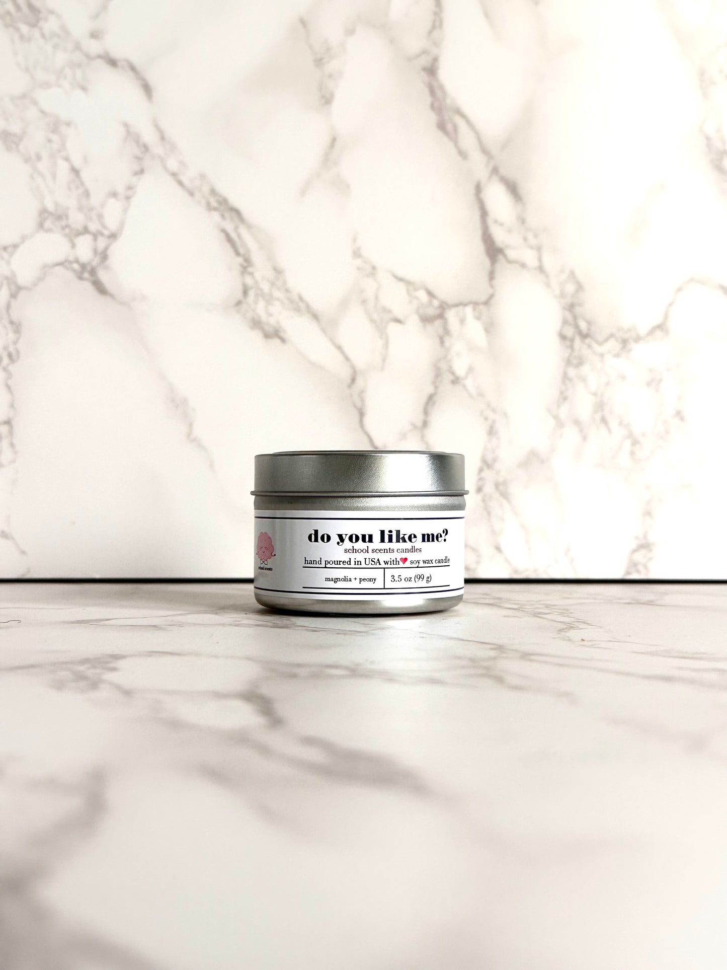 Silver travel tin candle labeled “do you like me" on a marble surface
