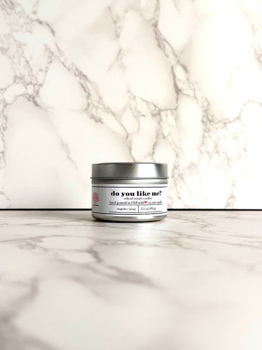 Silver travel tin candle labeled “do you like me" on a marble surface