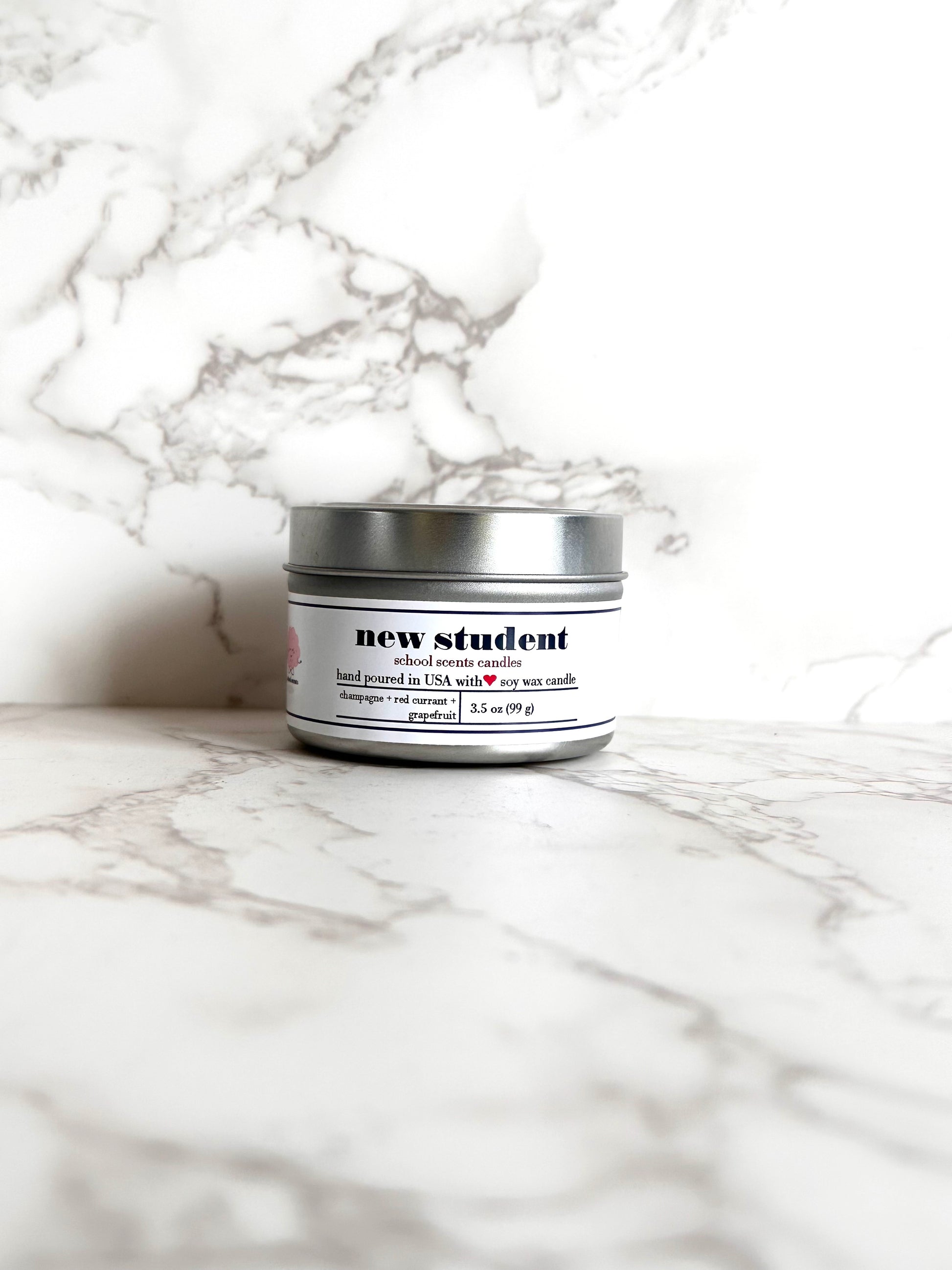 Silver travel tin candle labeled “New Student” on a marble surface