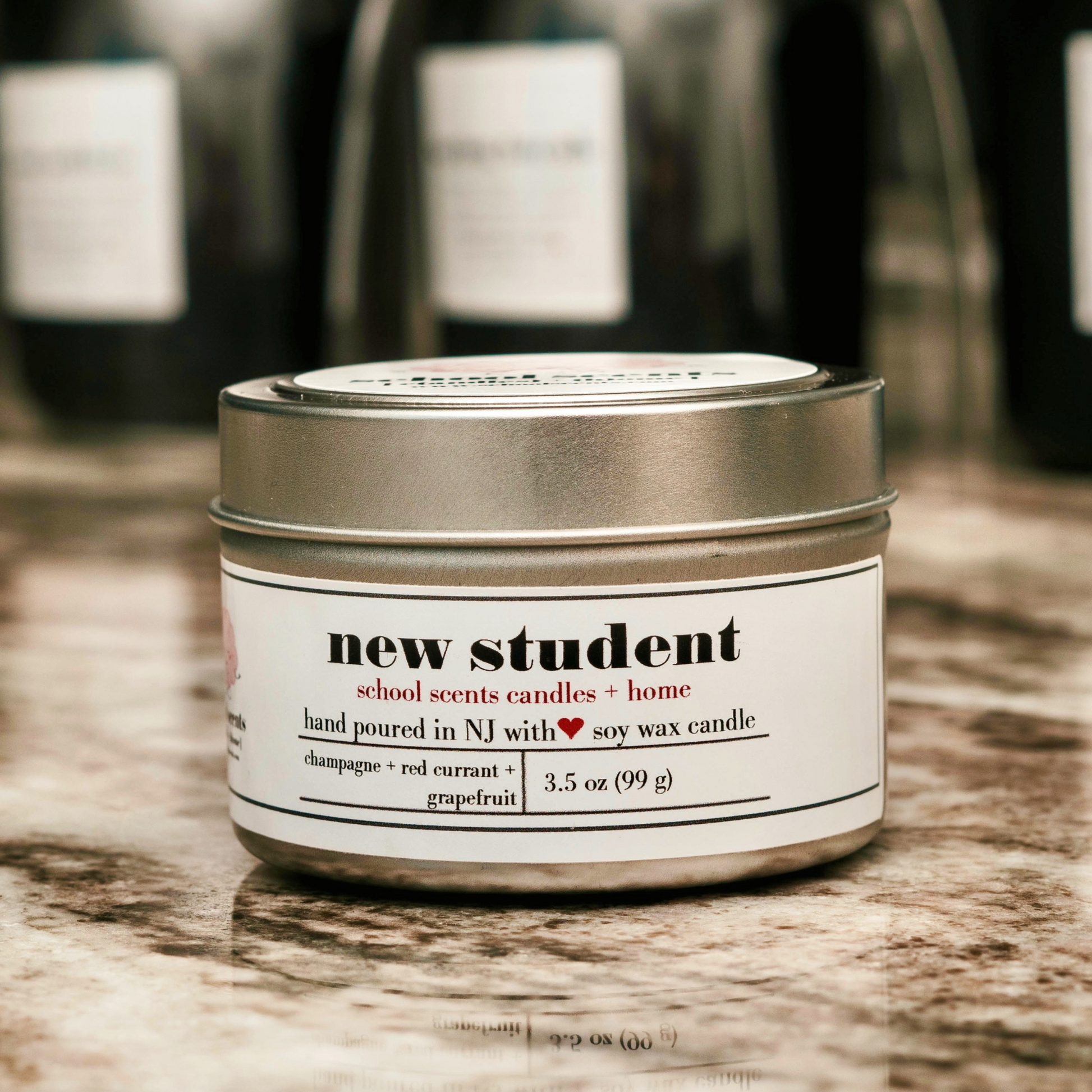 Close up of silver travel tin candle labeled “New Student” on a marble surface